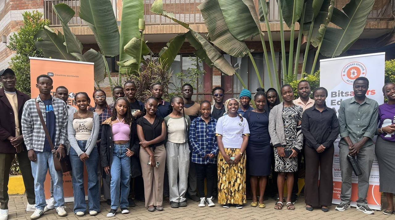 Group of about twenty students posing outdoors between Bitsavers Edunub Academy banners at the Trezor Academy Kenya cohort